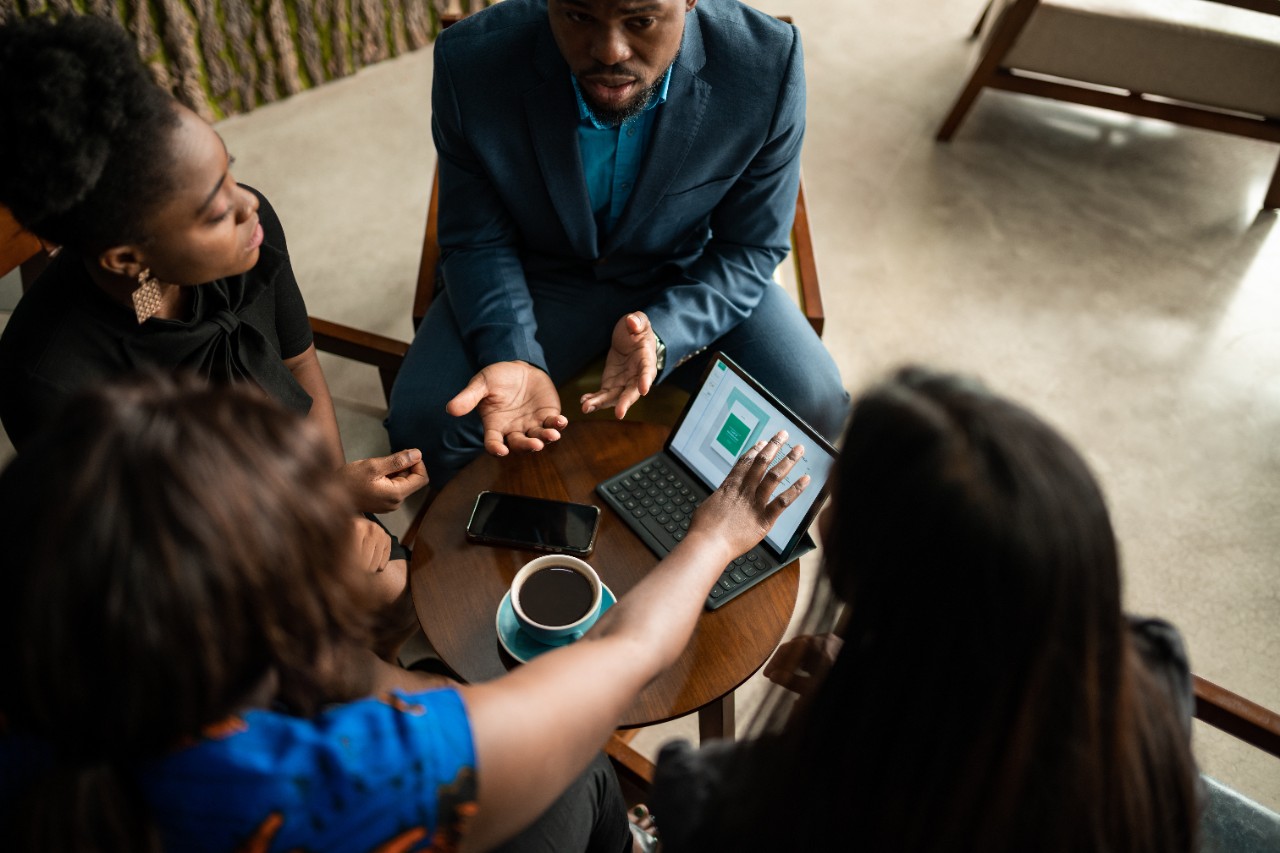 Focused group of young African businesspeople going through charts and paperwork during a meeting over coffee at a table in a modern office